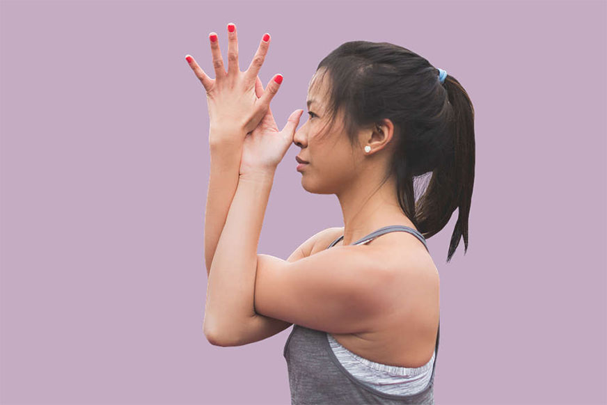 A woman performs a yoga pose, her hands clasped and arms extended, against a solid purple background.