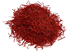 A pile of dried crimson saffron threads rests on a white background; a small, dark red cylindrical object is visible to the right.